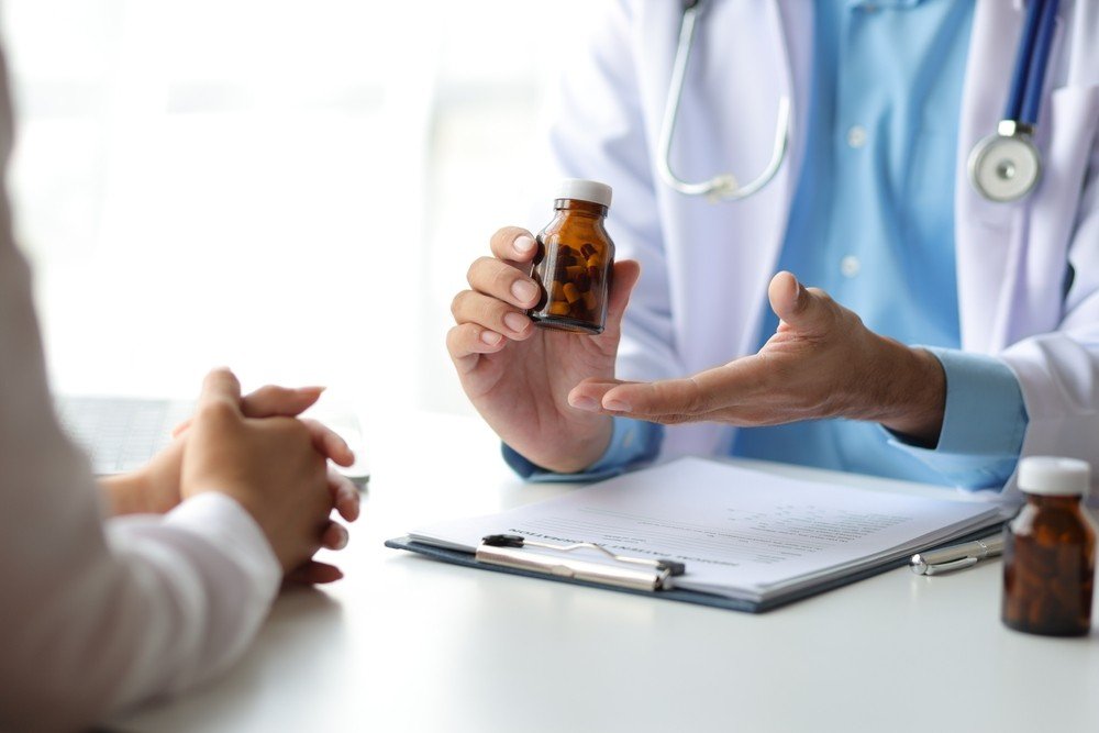 Pharmacist holding an amber medication bottle beside a clipboard while explaining a prescription