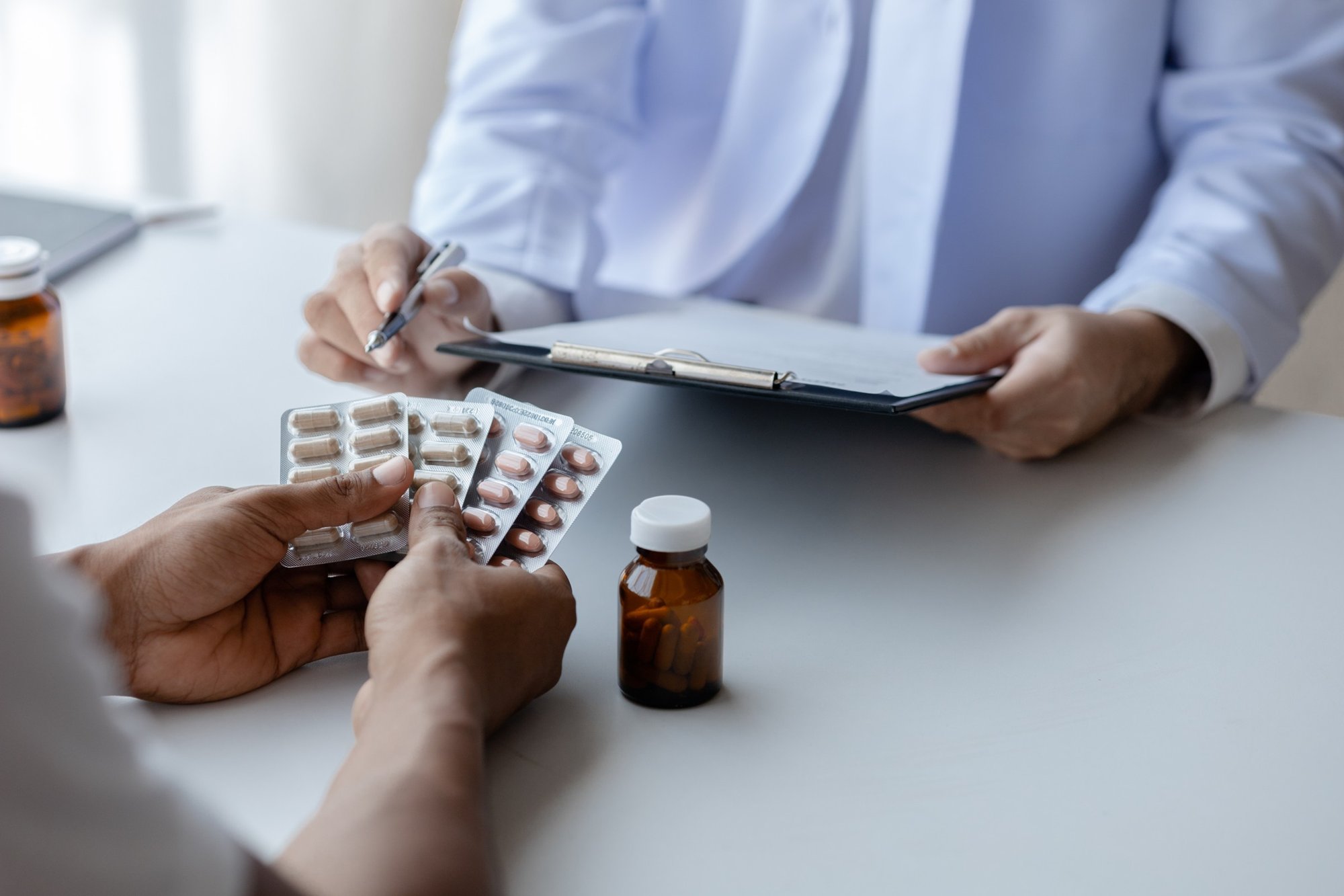 Patient holding blister packs of tablets while a provider writes notes on a clipboard