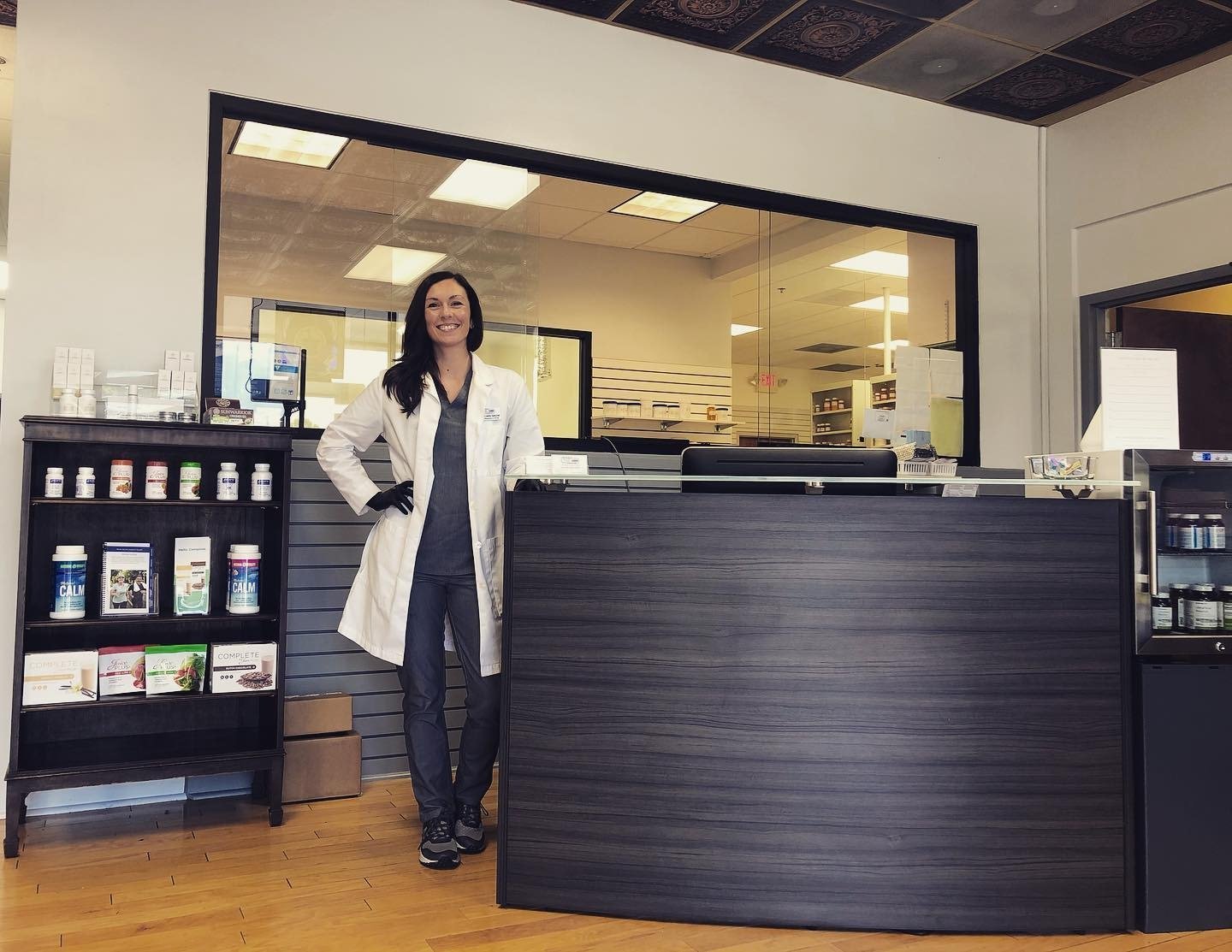 Pharmacist standing at the front counter of the Cherokee Custom Script Pharmacy lobby, serving patients in Johns Creek, GA