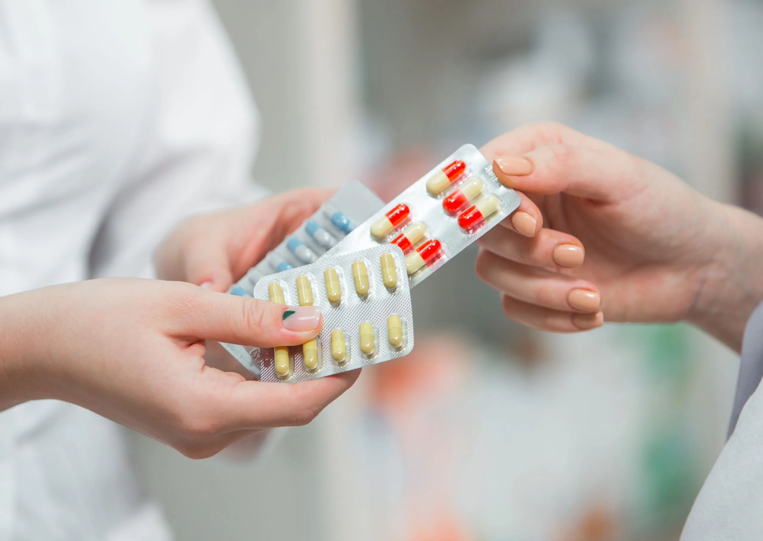 Pharmacist handing blister packs of red and yellow capsules to a customer