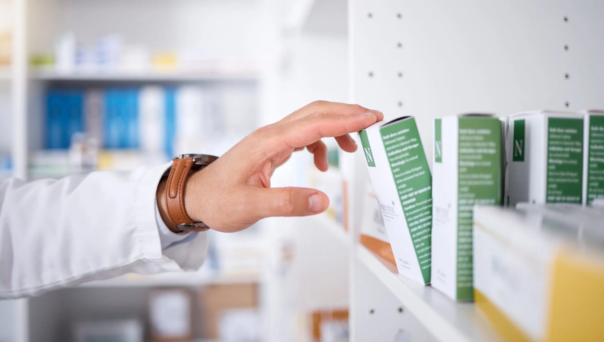 Pharmacist's hand selecting a medication box from a pharmacy shelf