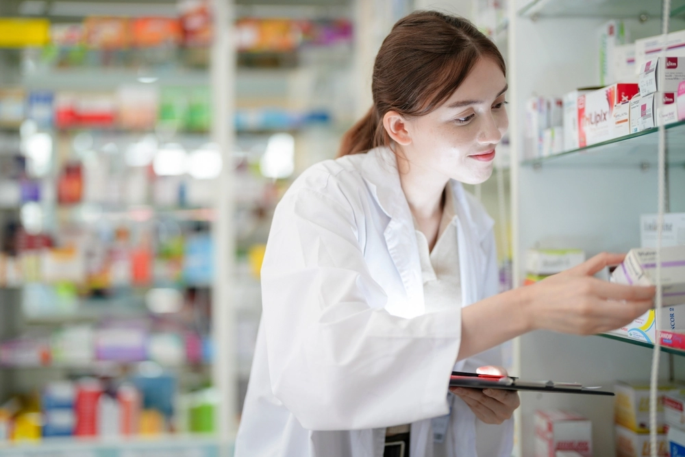 Pharmacist in lab coat selecting medication from pharmacy shelf