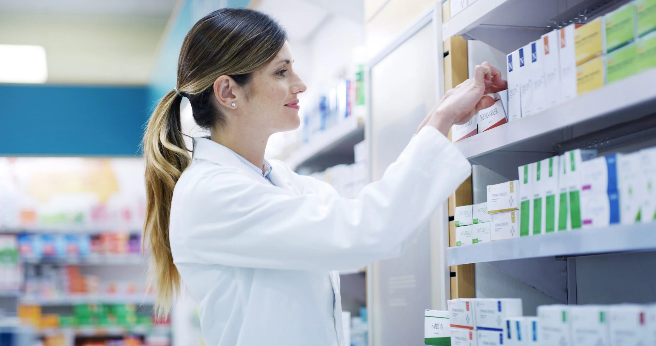Pharmacist in white coat checking medicine bottles on pharmacy shelf