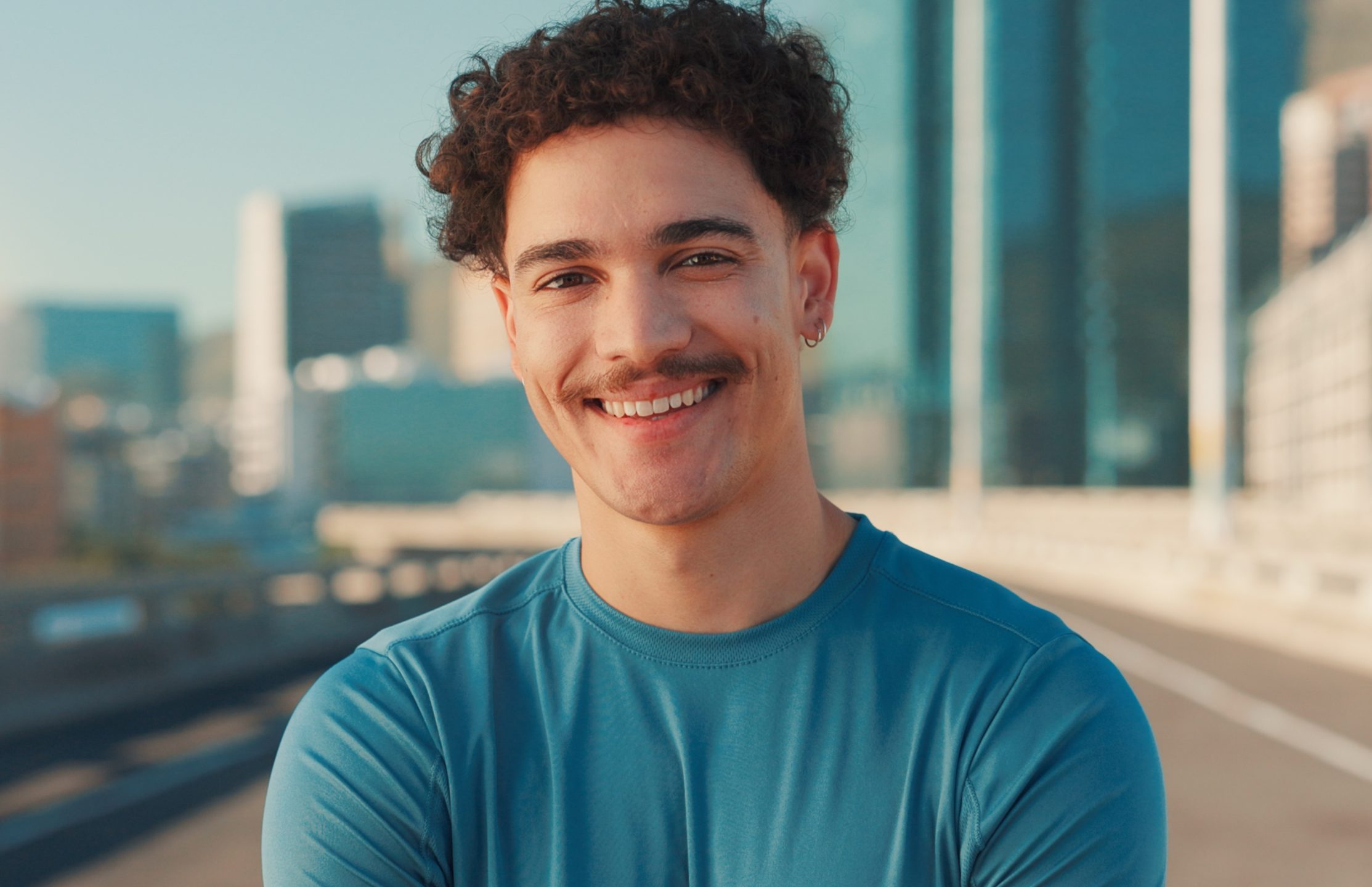 Smiling young man on a city overpass with downtown office towers behind him