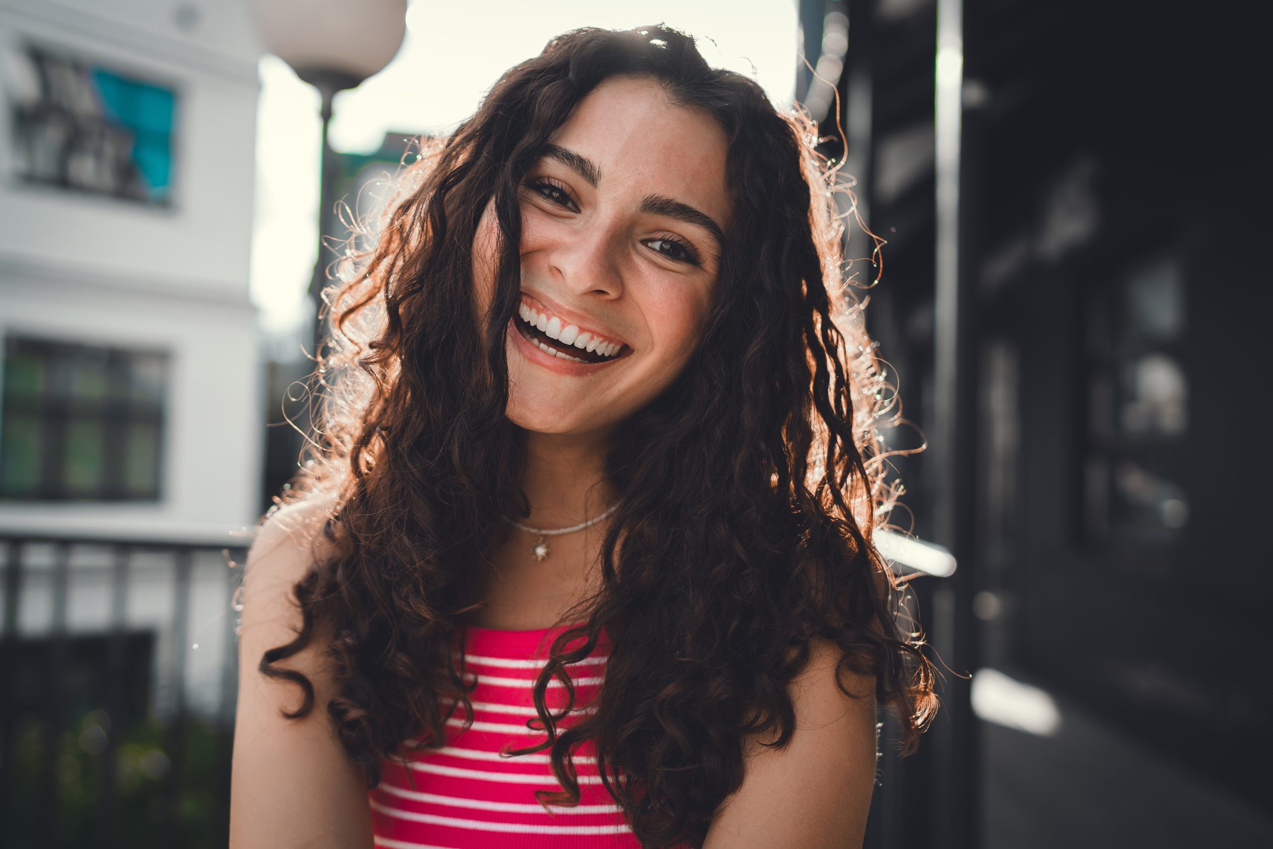 Smiling woman with curly hair standing on a sunny city street