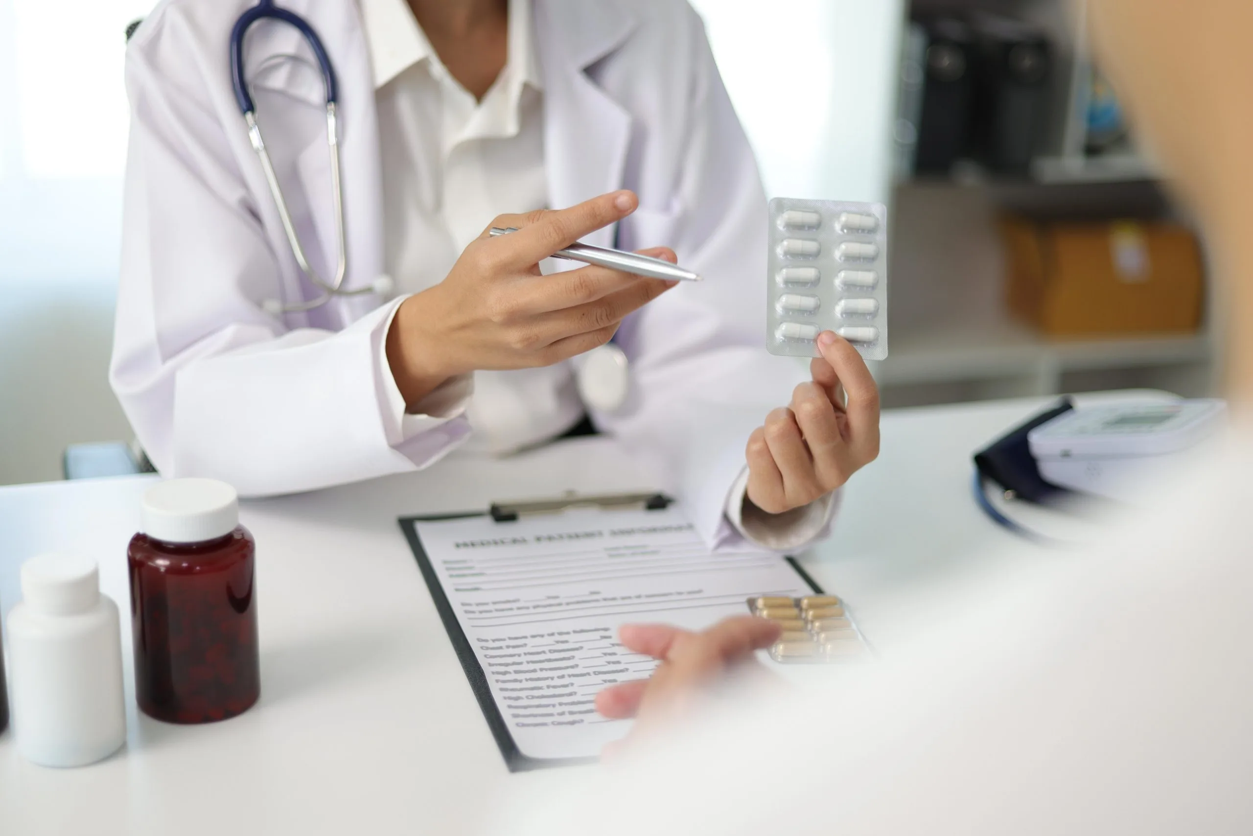 Healthcare provider holding medication blister pack and clipboard with prescription and compounded medications on desk