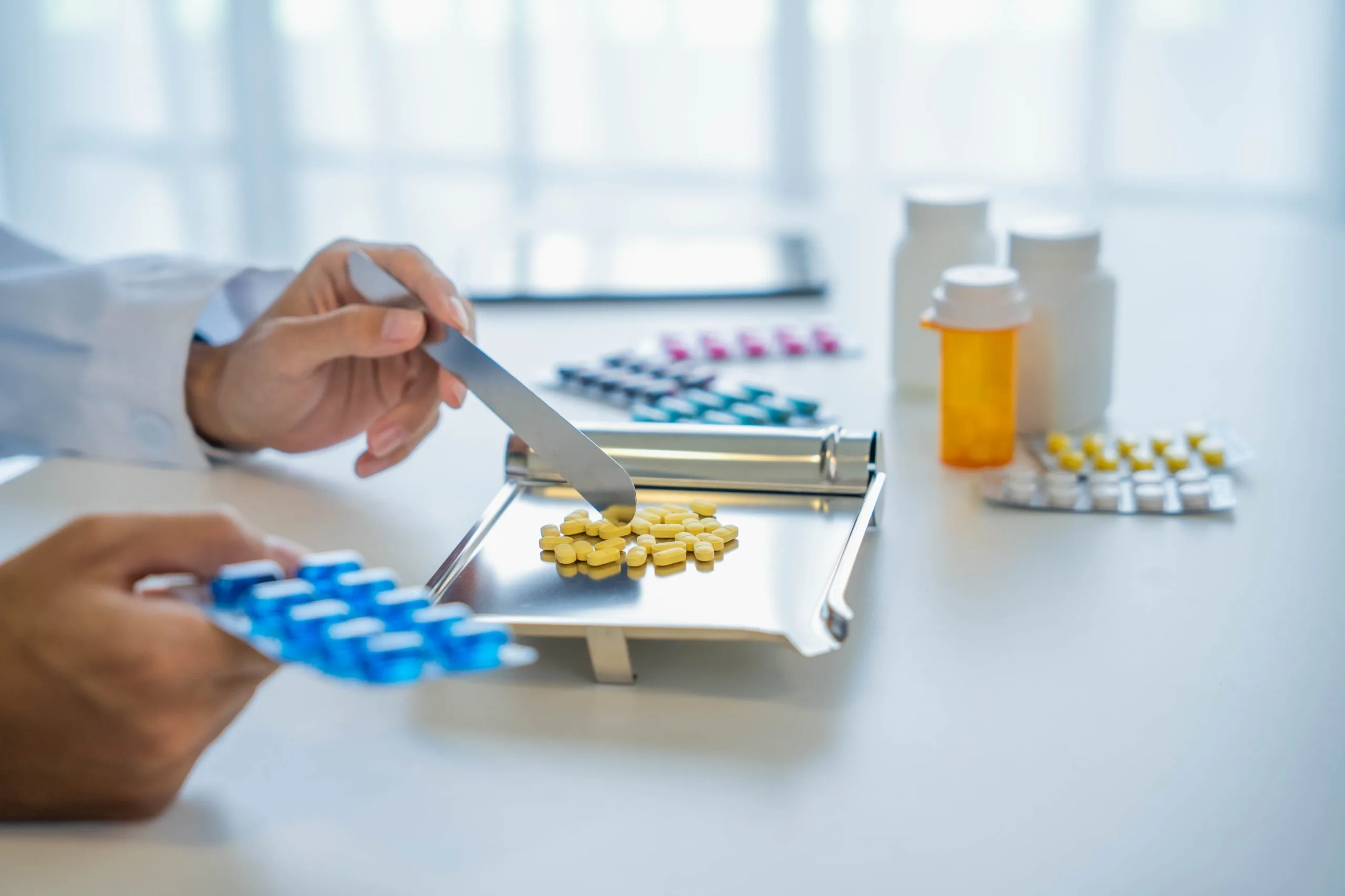 Pharmacist using a spatula to dispense yellow capsule medications onto a scale in a bright pharmacy setting