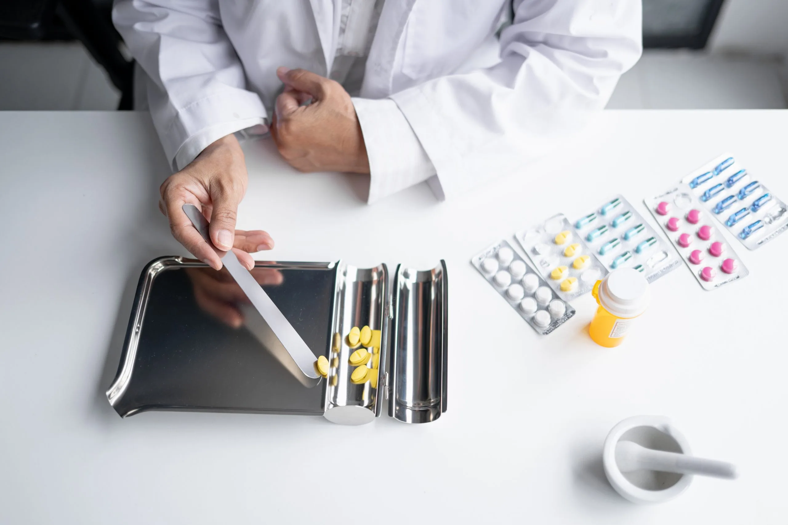 Pharmacist in white coat counting and arranging prescription pills from containers and blister packs on a white surface