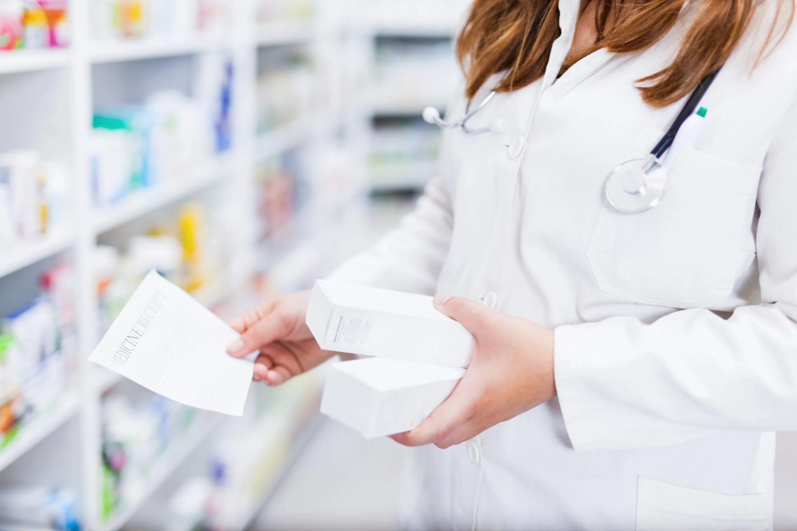 Pharmacist in white coat holding medication bottle and prescription label in front of pharmacy shelves