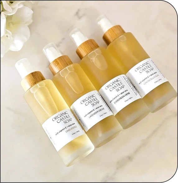 Four bottles of Organic Cascade Soap with white and gold labels arranged on marble surface with white flowers