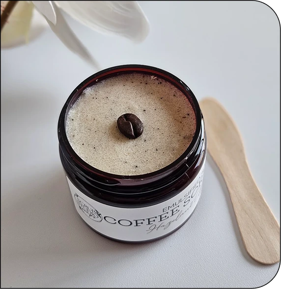 CNT coffee scrub jar with tan exfoliating product and coffee bean on top, wooden applicator beside it