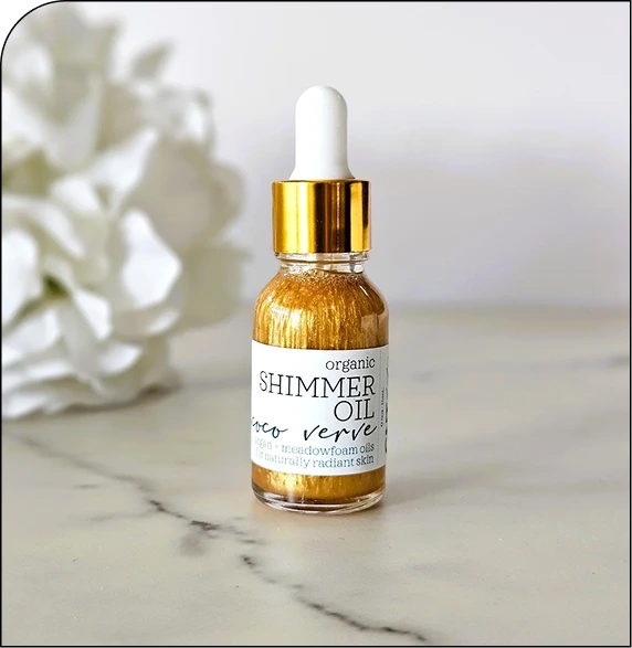 Organic Shimmer Oil bottle with gold dropper cap on marble surface beside white flowers