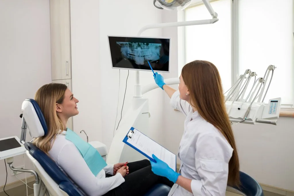 Dentist pointing to a dental x-ray on a monitor while explaining results to a smiling patient