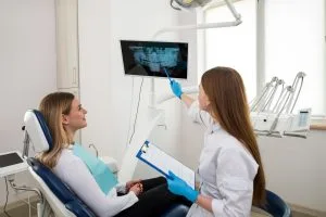 Dentist pointing to a dental x-ray on a monitor while explaining results to a smiling patient