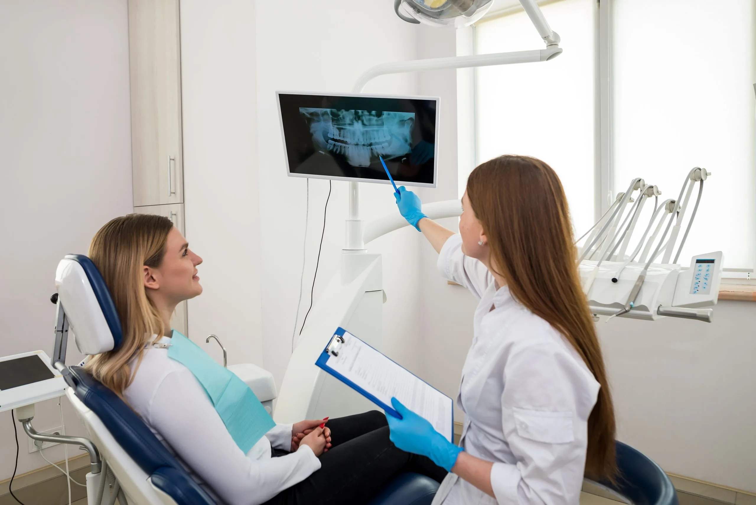 Dentist pointing to a dental x-ray on a monitor while explaining results to a smiling patient