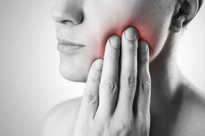 Person pressing a hand to a sore jaw, a common TMD symptom checked at a first consultation in Collegeville, PA