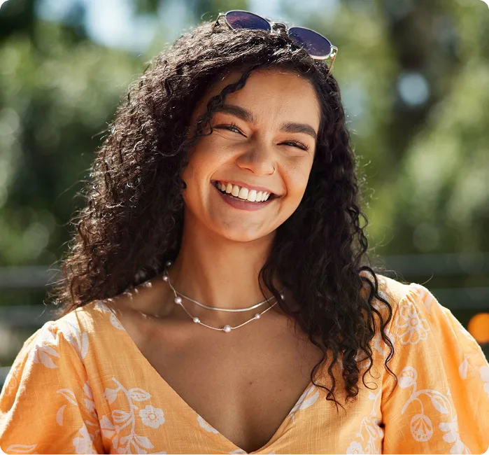 Woman with curly dark hair smiling outdoors in yellow patterned shirt with sunglasses on head