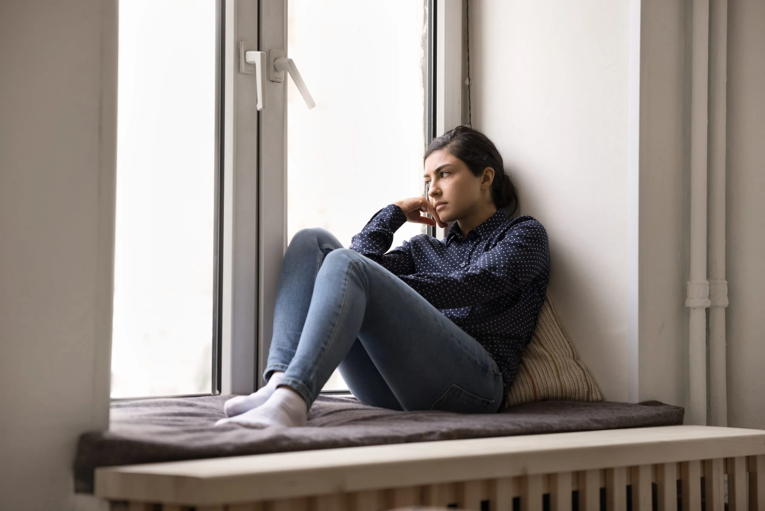Woman sitting on a windowsill looking thoughtful, used to illustrate betrayal trauma recovery