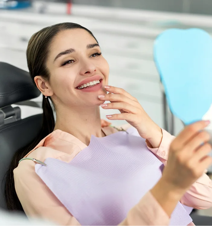 Patient in dental chair admiring her smile in mirror after exam and cleaning