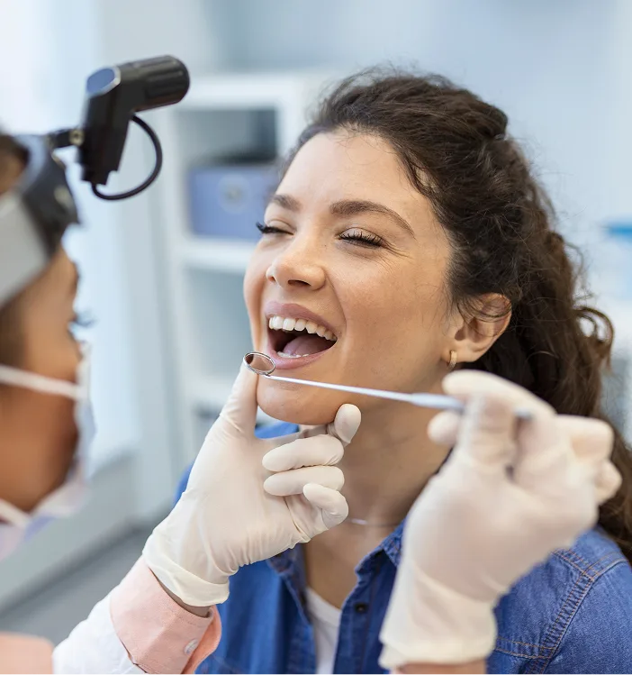 Dentist performing oral cancer screening on patient with intraoral camera and mouth mirror in dental office
