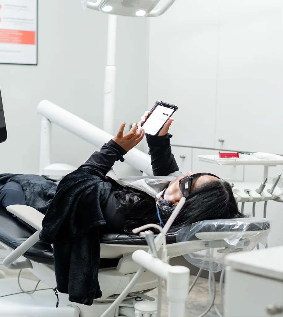 Patient in dental chair viewing treatment plan on smartphone at Dentcare Now