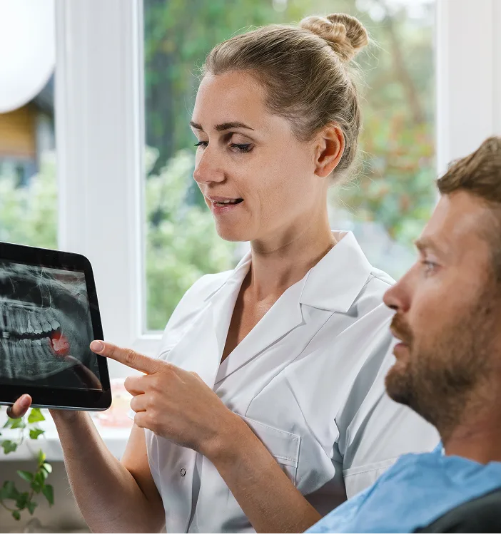 Dentist pointing to wisdom teeth X-ray on tablet while discussing results with male patient