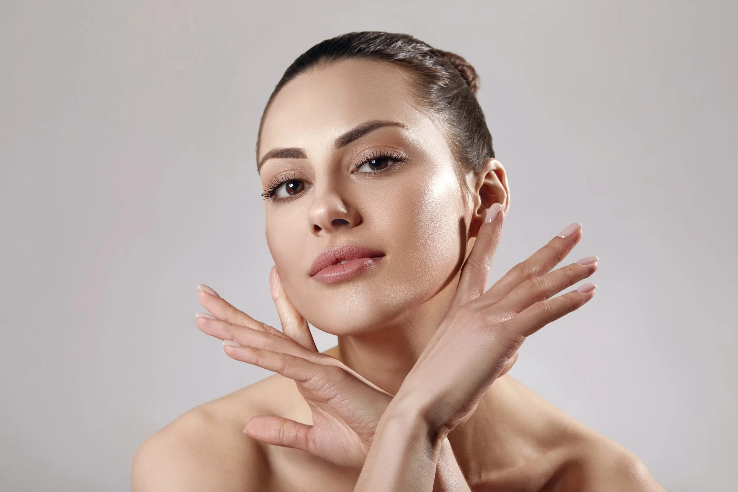 Woman touching her neck and jawline against a neutral background