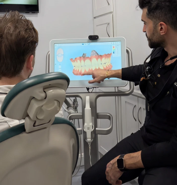 Dentist pointing to digital teeth model on monitor while patient sits in dental chair