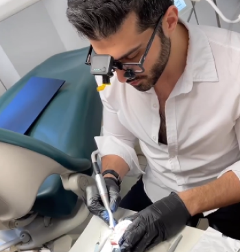 Dentist in white coat and protective eyewear performing laser-assisted treatment on patient's tooth