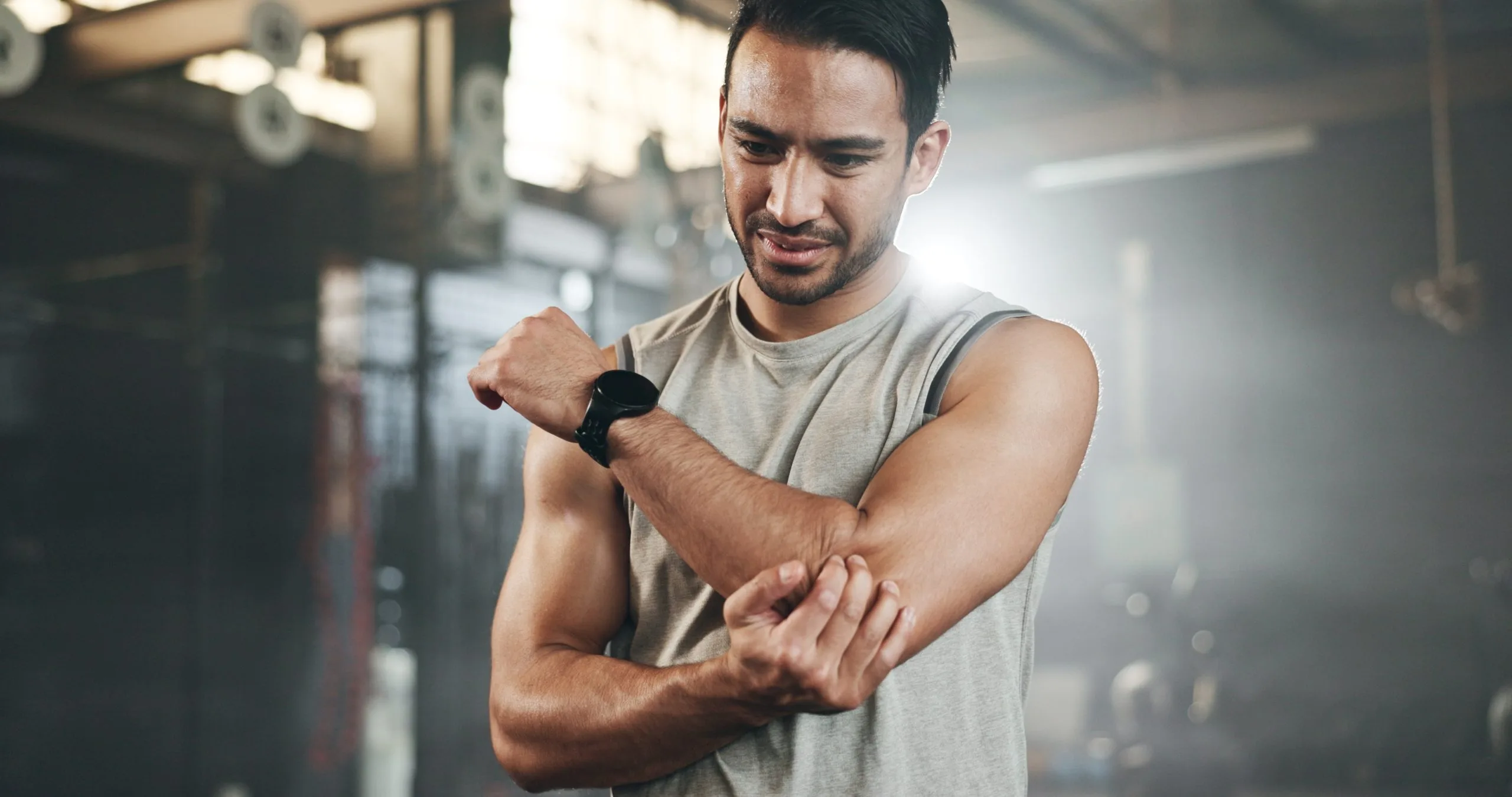 Man at gym holding his elbow in pain while wearing a wrist support band
