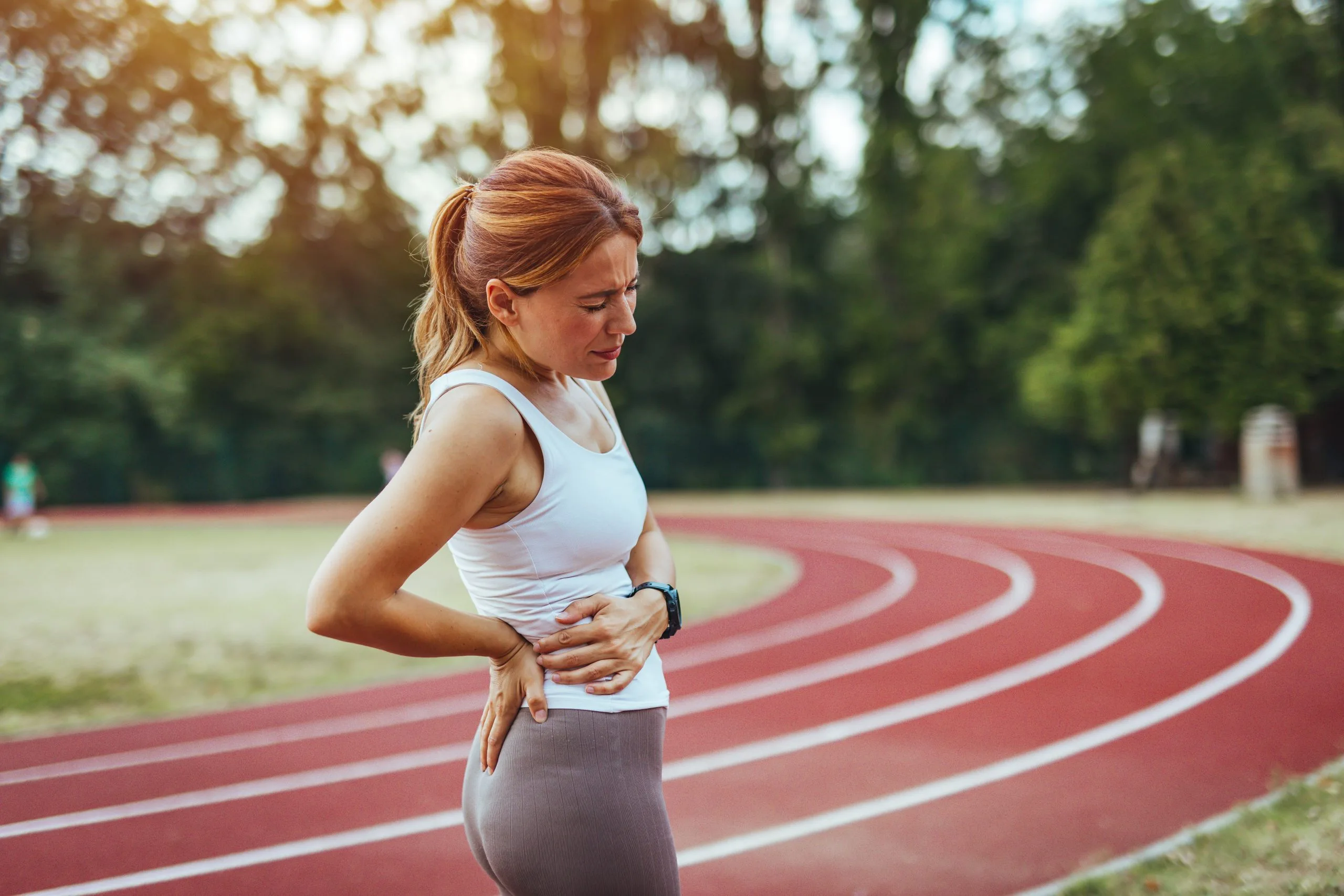 Woman holding her hip while standing on a running track, experiencing pain