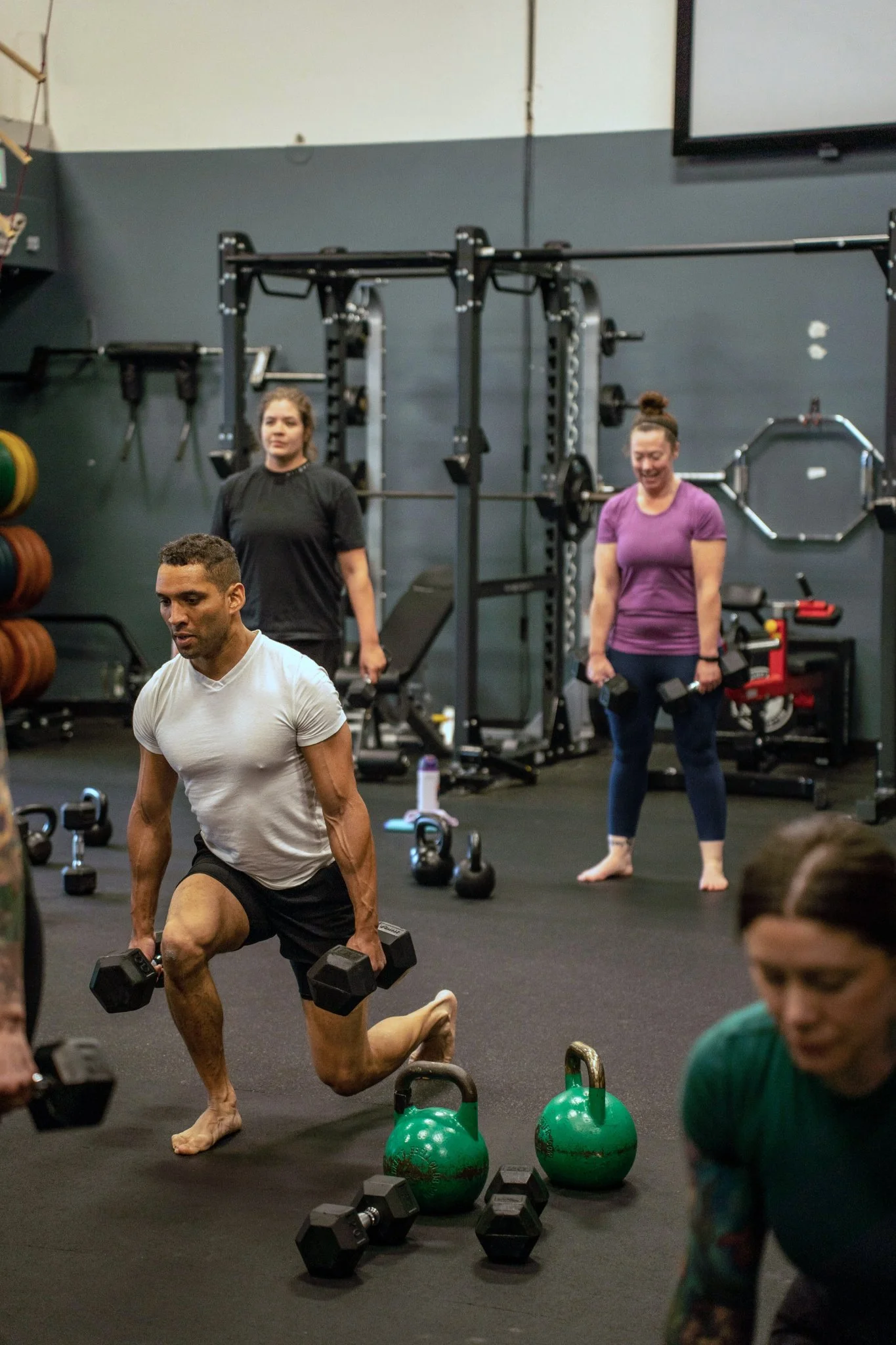 Group fitness class at Evolution Healthcare & Fitness with participants exercising with dumbbells and kettlebells in a gym setting