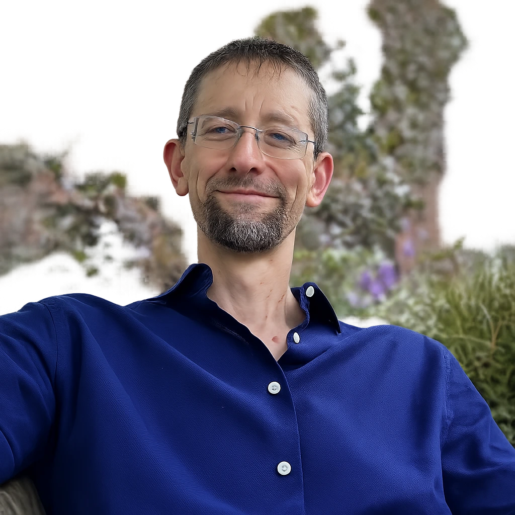 Man wearing glasses and blue button-up shirt smiling outdoors with cacti and desert landscape behind him
