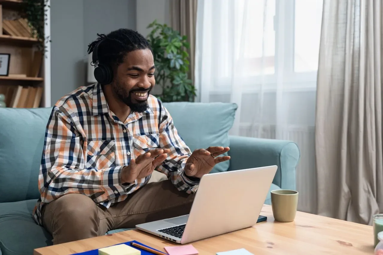 Smiling man wearing headphones talking with his therapist on a laptop video call from his living room