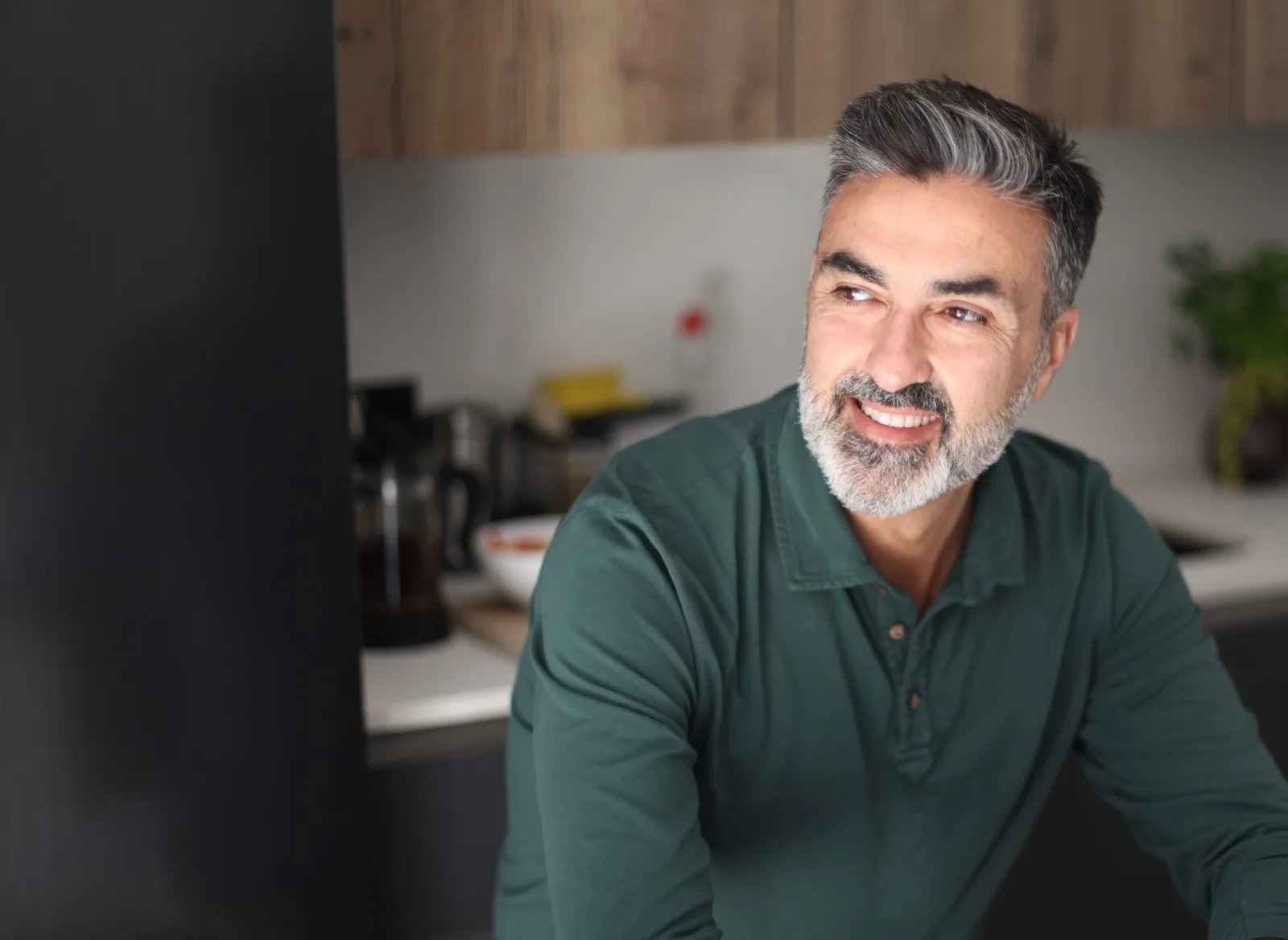 Smiling middle-aged man with gray hair and a beard sitting at his kitchen table at home