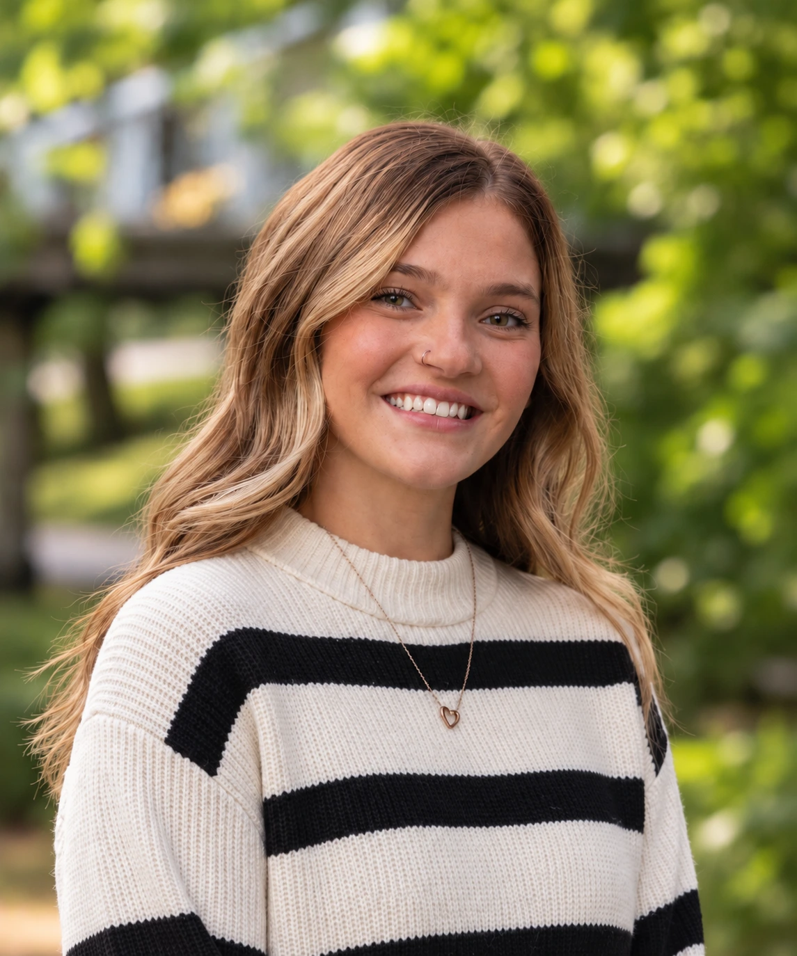 Professional headshot of a smiling woman with long brown hair wearing a cream and black striped sweater outdoors