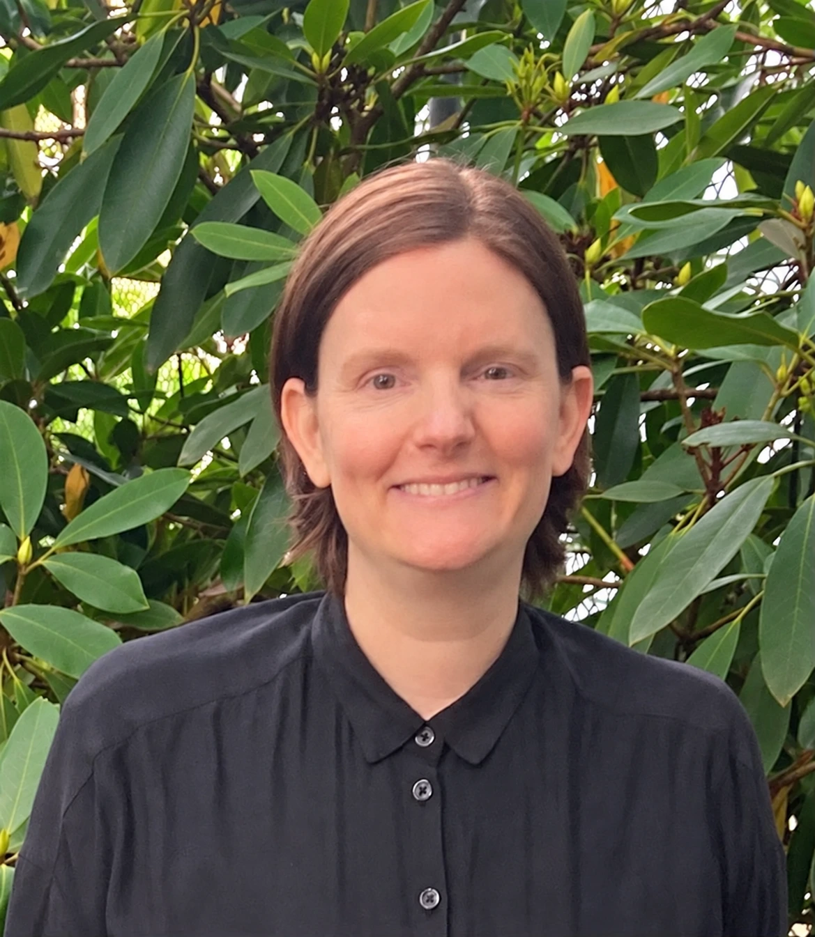 Team member Rebecca smiling at camera with green foliage background
