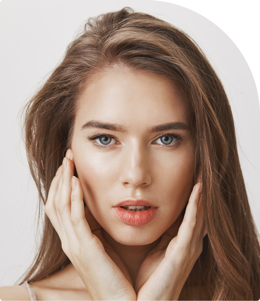 Woman with brown hair touching her face with both hands, looking at camera