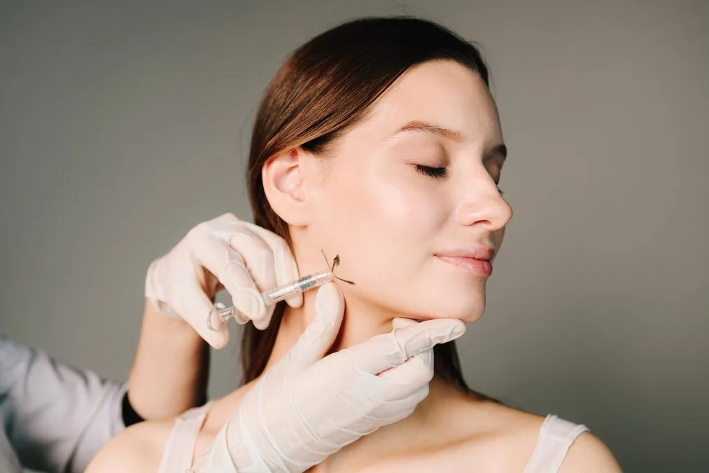 Provider in gloved hands administering Botox injection to patient's jawline