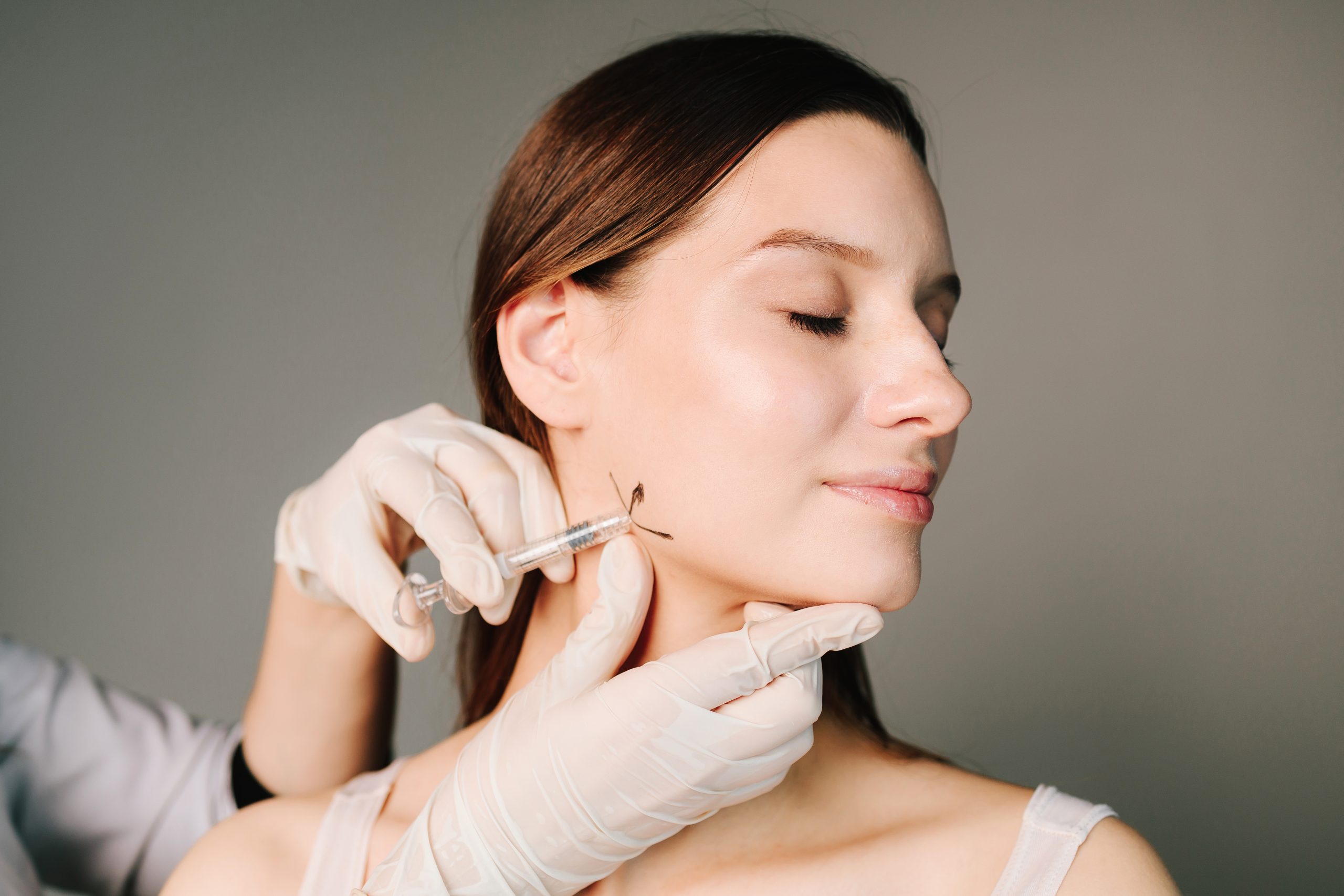 Provider in gloved hands administering Botox injection to patient's jawline