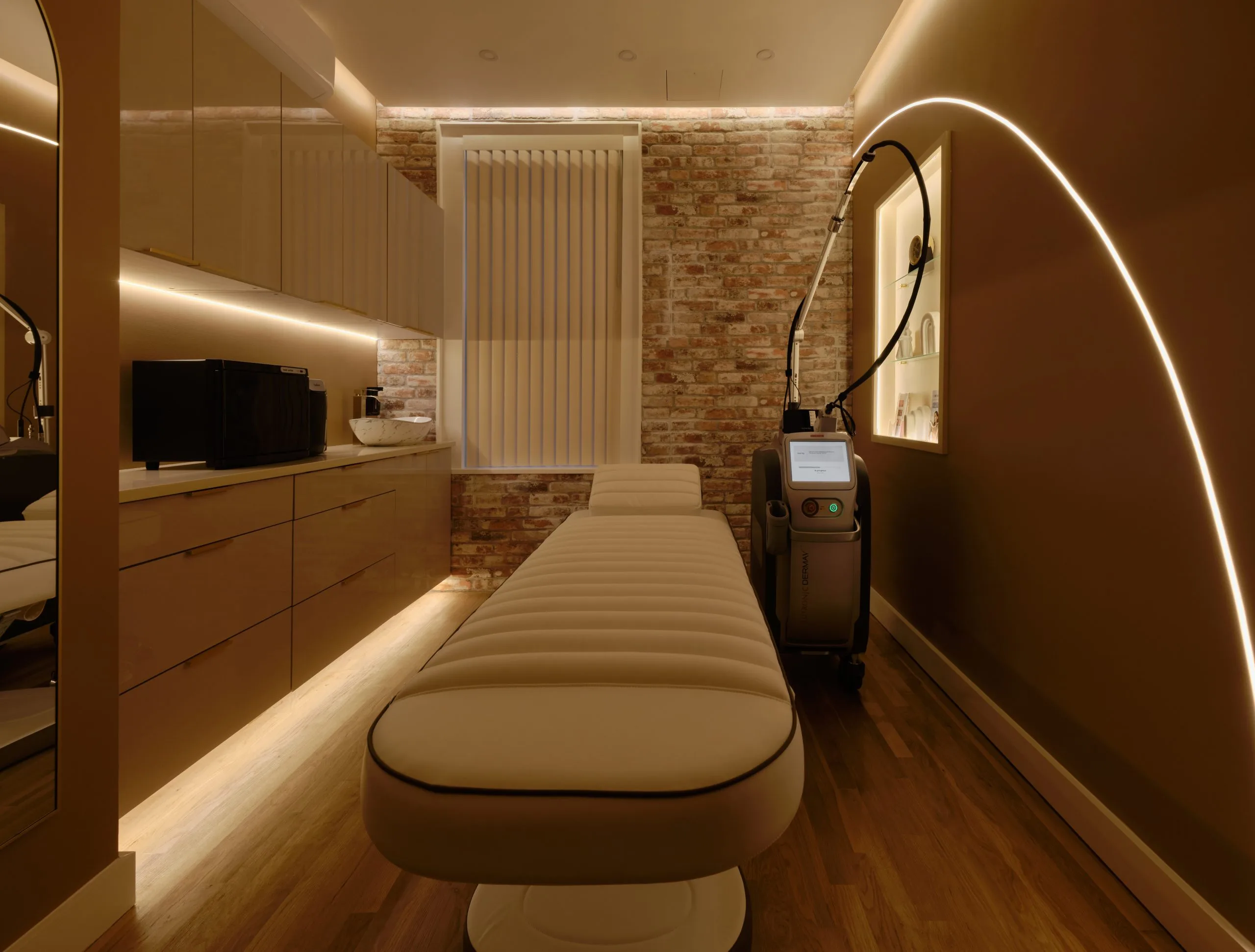 Treatment room at La Reservé Aesthetics & Wellness in Soho with a padded treatment bed, laser device and exposed brick wall