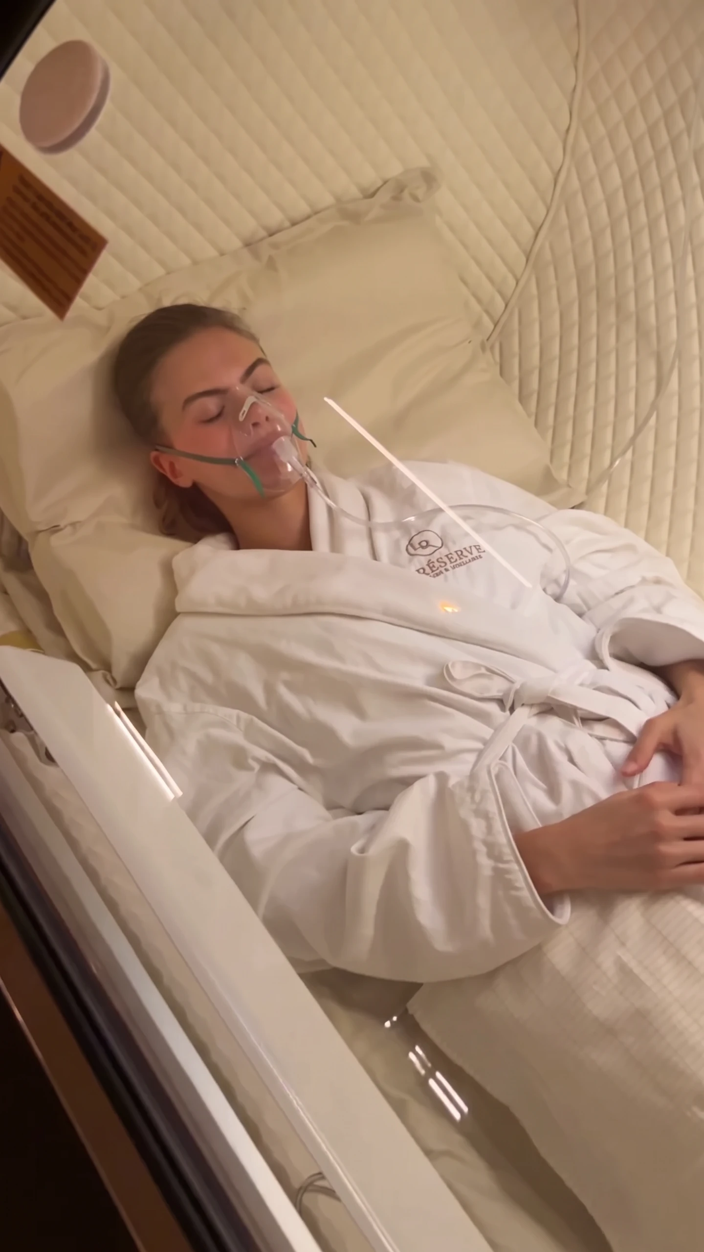 Client in a La Reservé robe resting with an oxygen mask inside a hyperbaric chamber