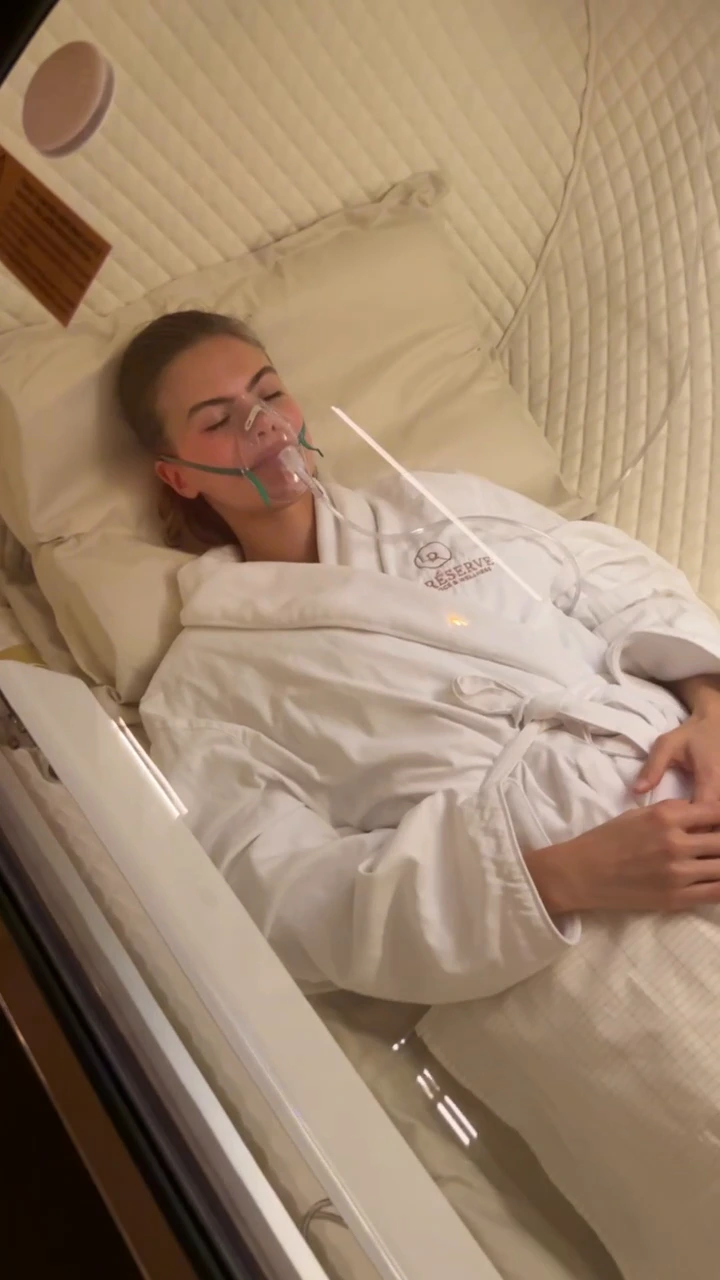 Client in a La Reservé robe resting with an oxygen mask inside a hyperbaric chamber