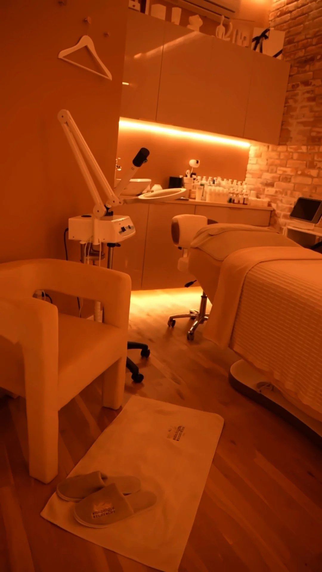 La Reservé Aesthetics treatment room with orange ambient lighting, treatment chair, medical device with articulating arm, and product display shelf