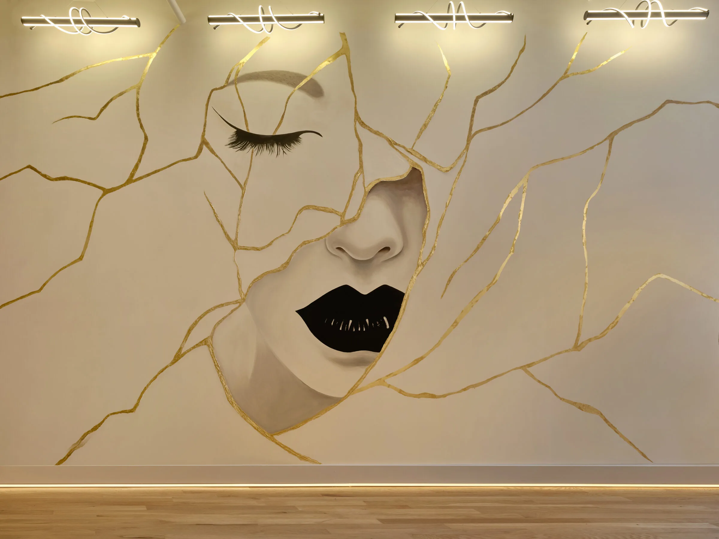 Abstract mural of a woman's face with gold vine designs and linear lighting fixtures in La Reservé Aesthetics and Wellness Main Office