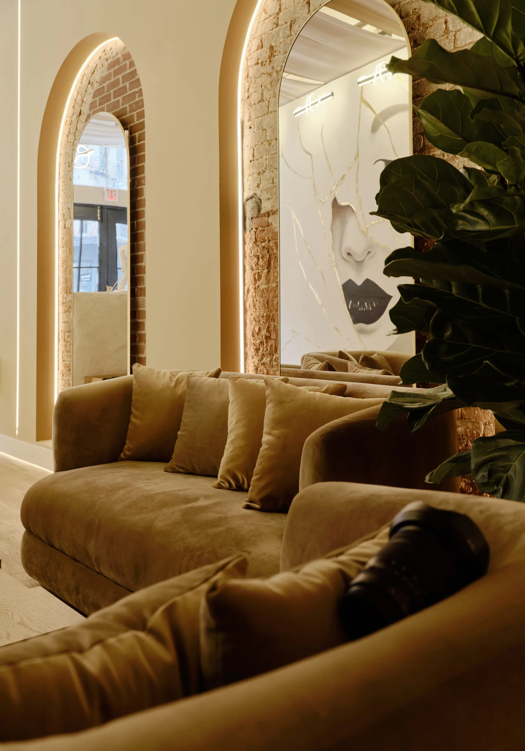 La Reservé Aesthetics and Wellness waiting area with tan curved seating, illuminated arched mirrors, exposed brick, and potted plants