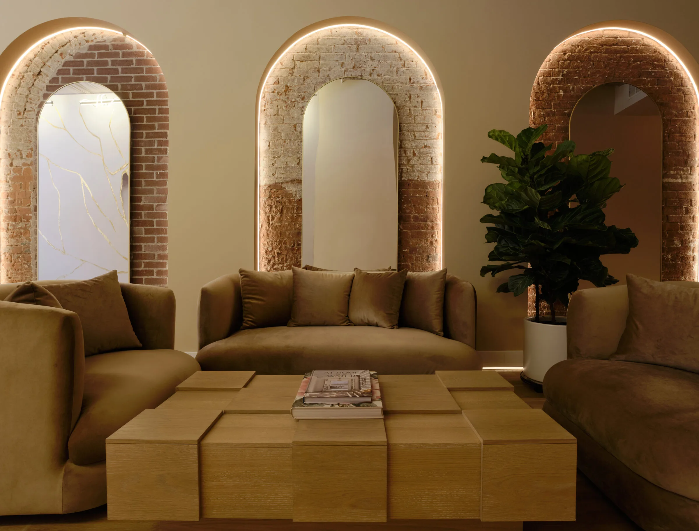 Luxury waiting area with arched brick alcoves, gold sofas, wooden coffee table, and green plant at La Reservé Aesthetics and Wellness