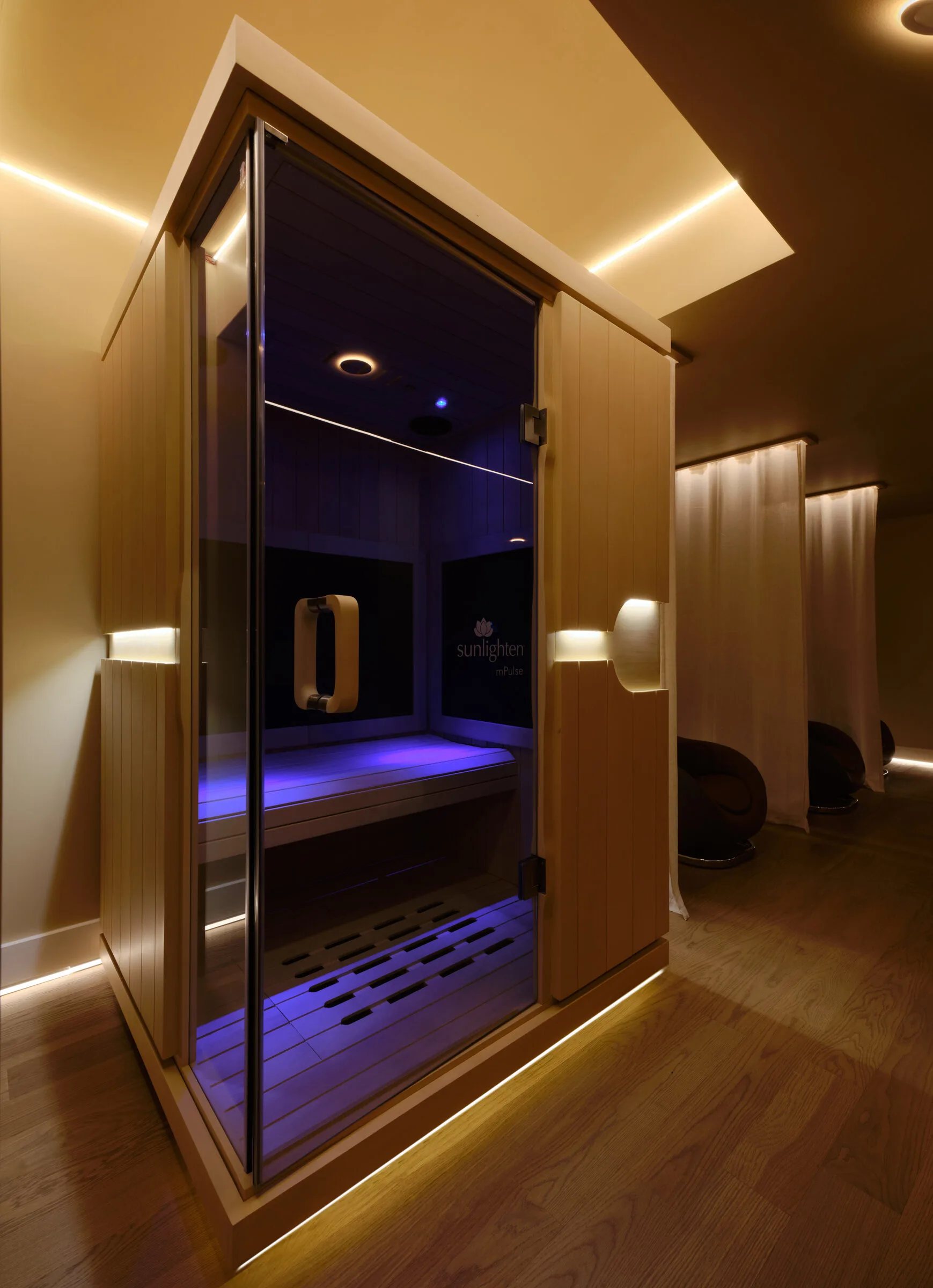 Modern sauna cabin with wood frame, glass door, blue-lit interior, and ambient lighting in La Reservé Aesthetics wellness center