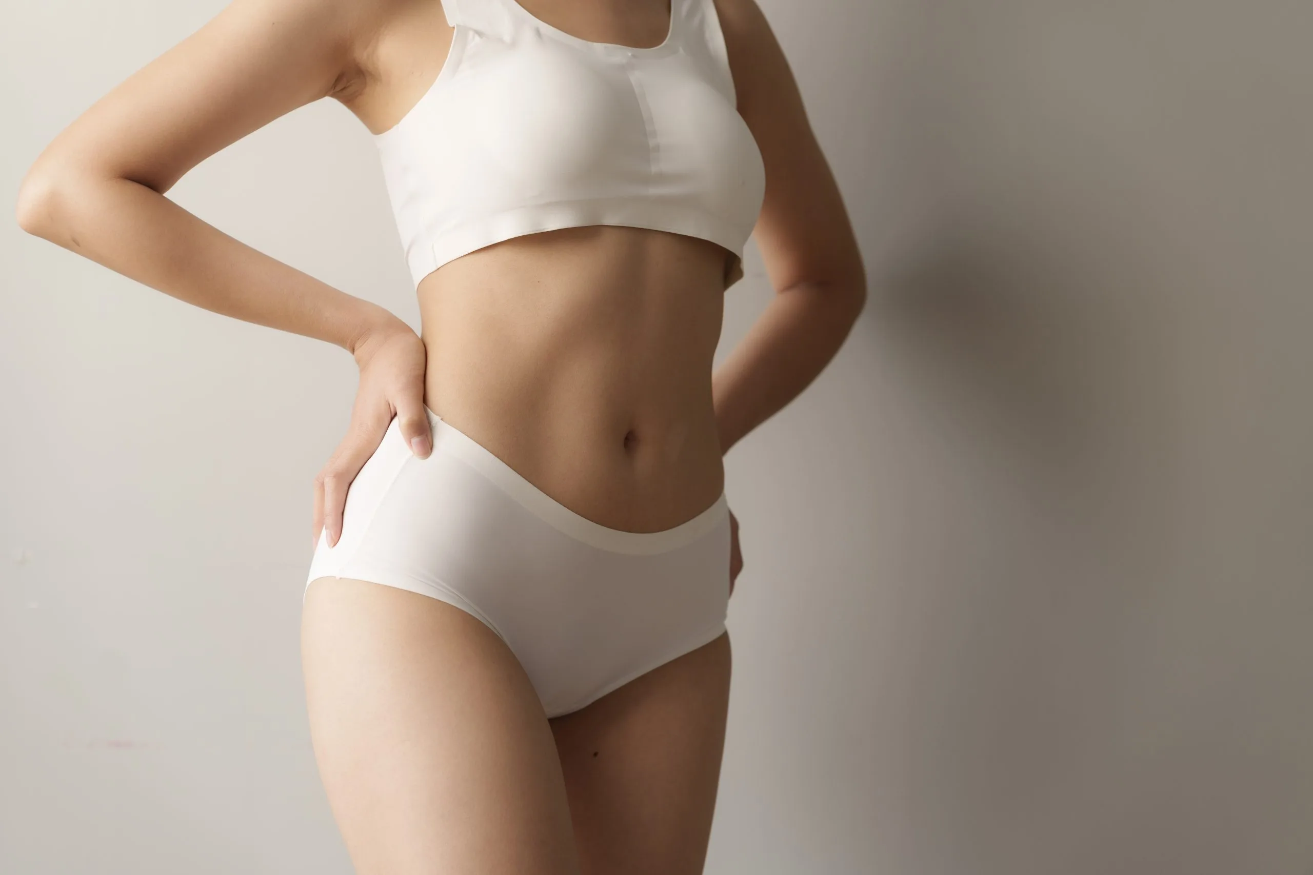 Woman in white sports bra and briefs touching abdomen