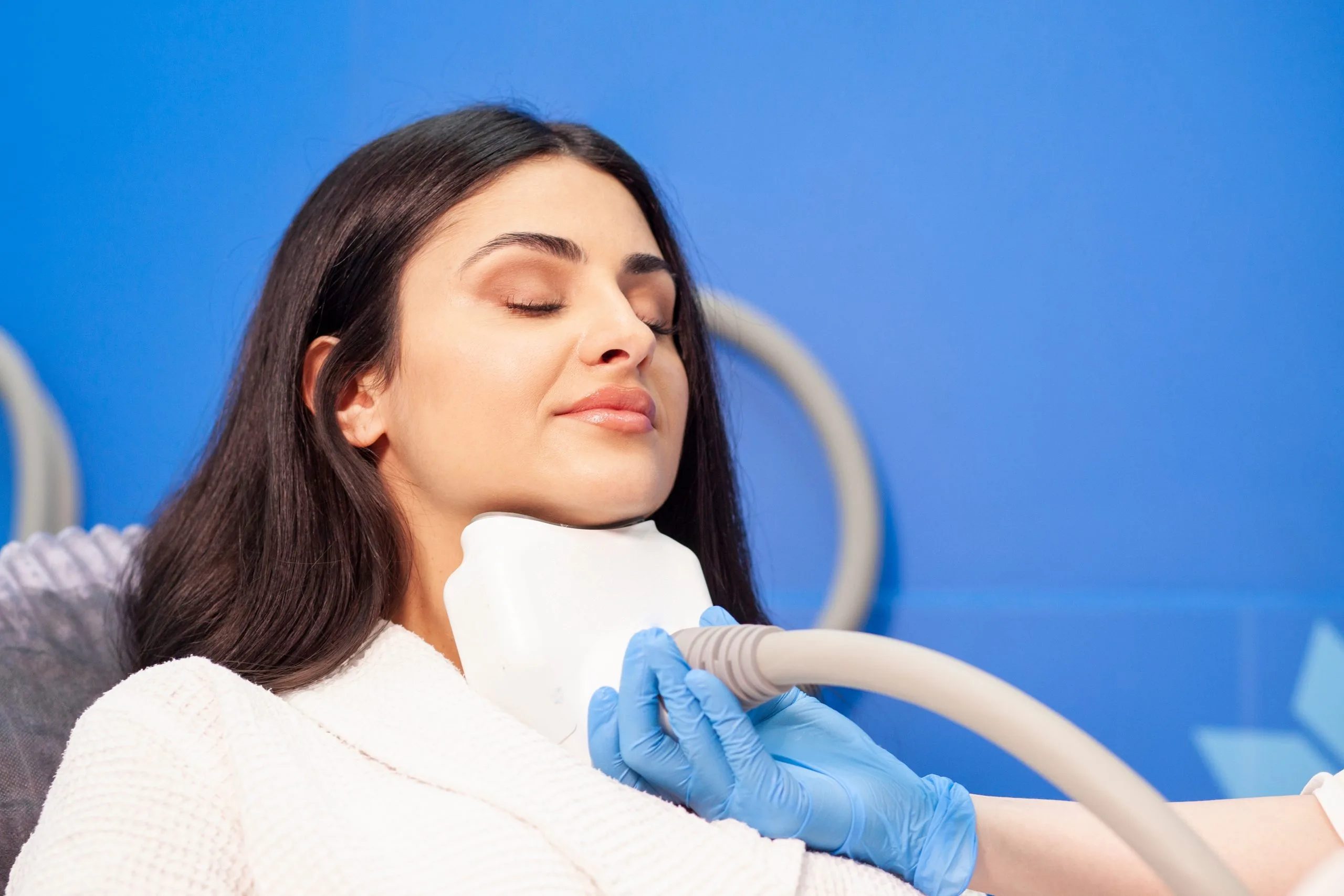 Practitioner in blue gloves applying CoolSculpting device to woman's chin and neck area